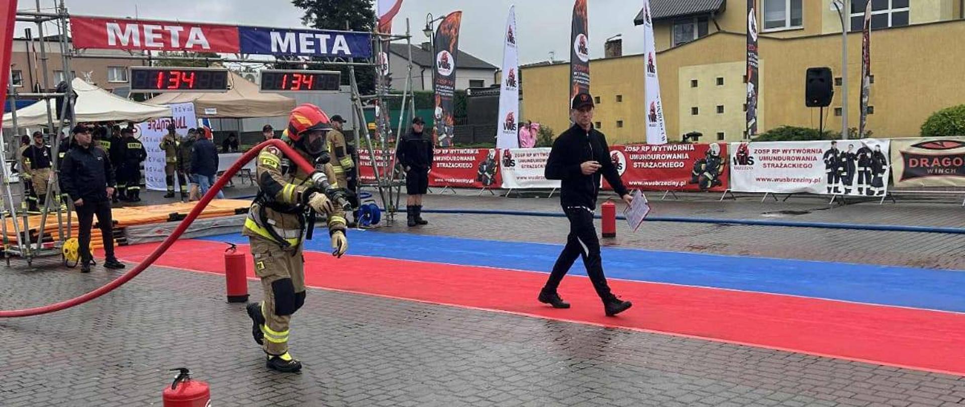 Na zdjęciu strażak w pełnym bojowym umundurowaniu podczas wykonywania czynności na zawodach sportowych.