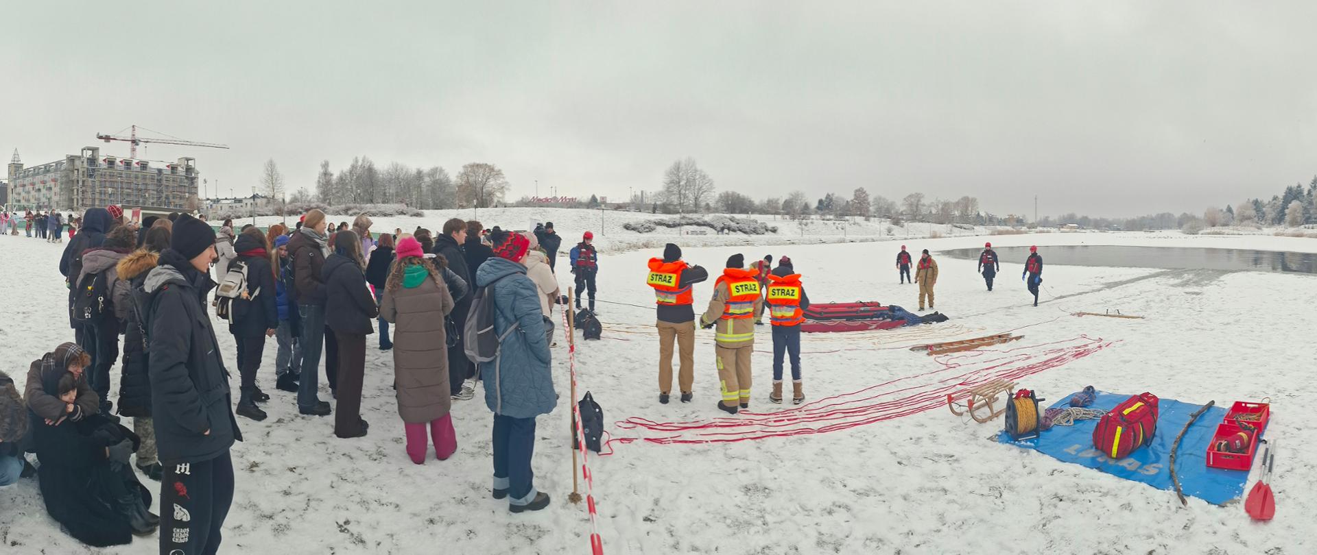 Strażacy demonstrują techniki ewakuacji osoby z przerębla przy użyciu lin ratowniczych i sprzętu specjalistycznego podczas pokazu na zamarzniętym akwenie