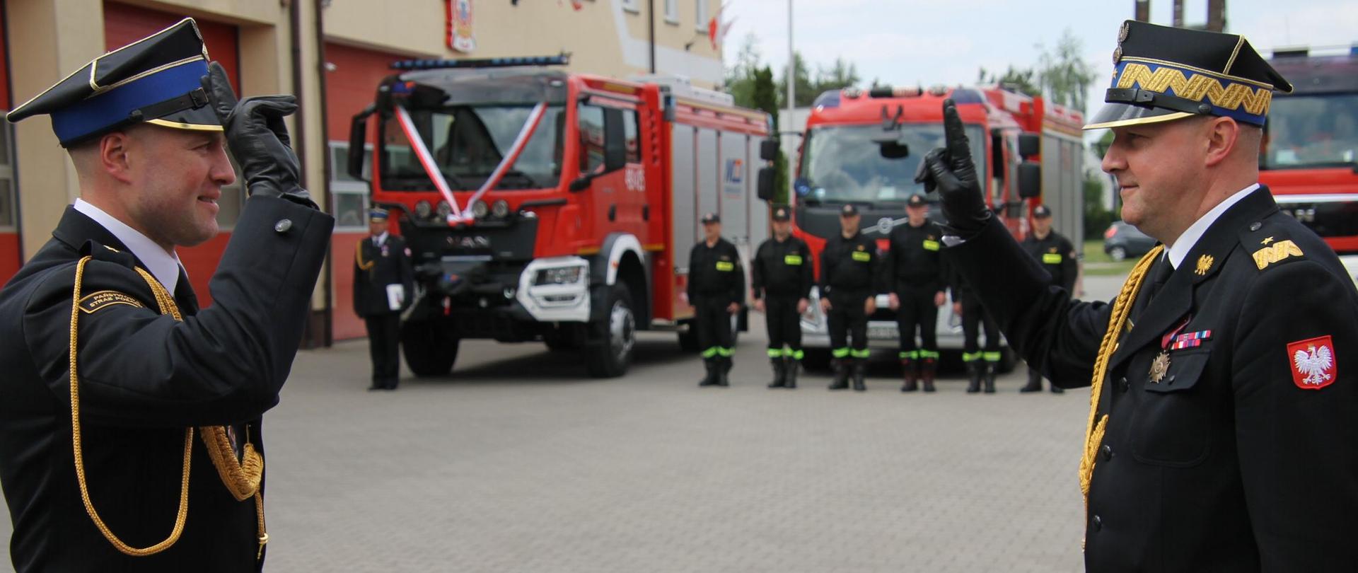 składanie meldunku komendantowi podczas uroczystości, w tle samochody strażackie