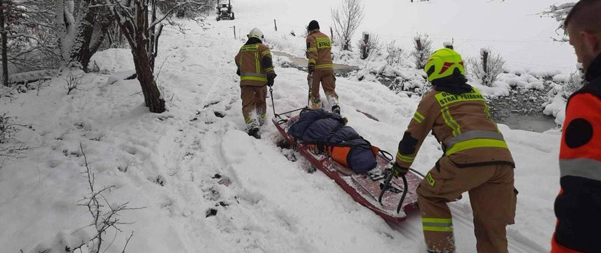 Transport poszkodowanego przez zasypaną śniegiem drogę.