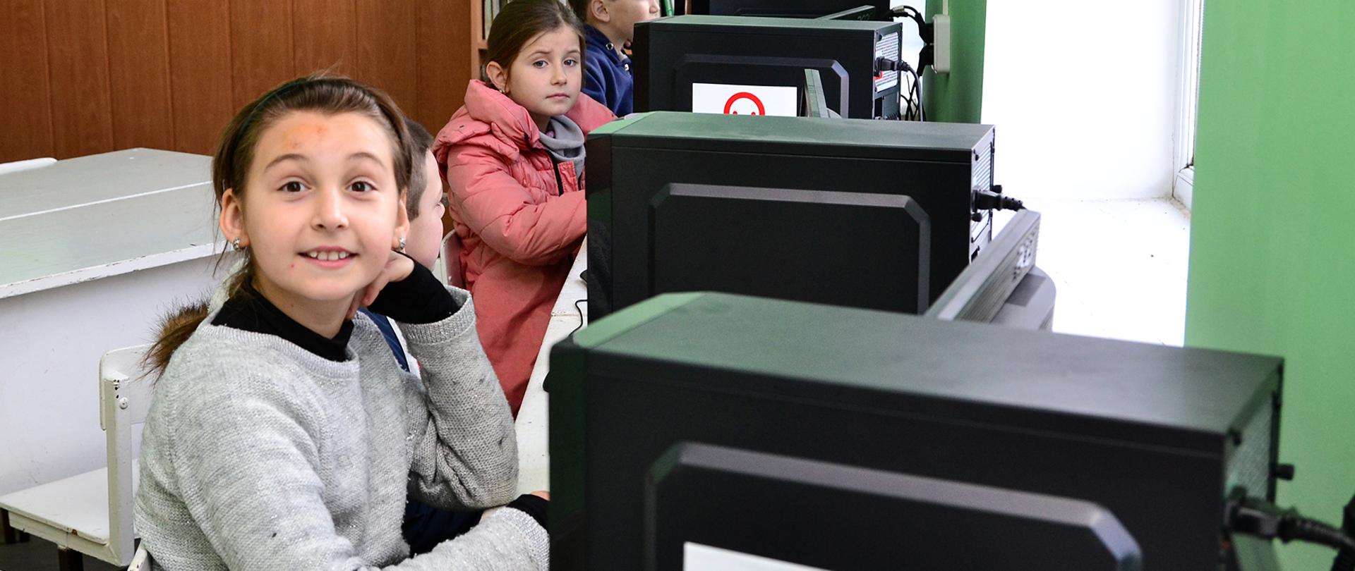dzieci siedzące przy komputerach oznakowanyc znakiem Polska pomoc