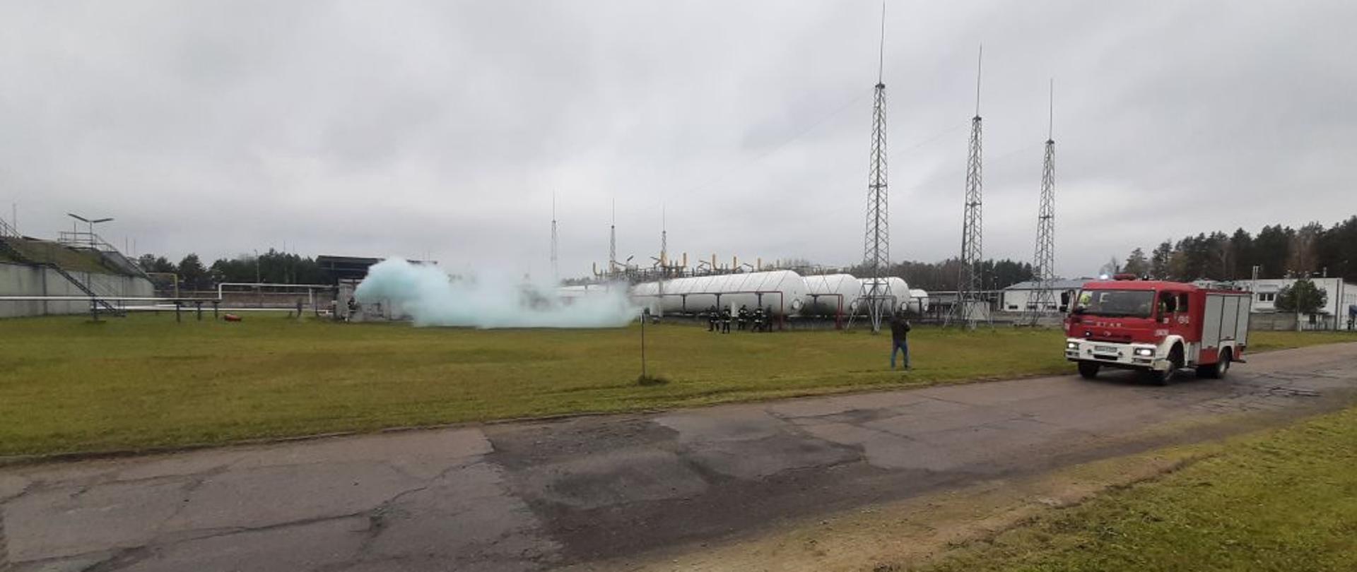 Na tle zbiorników z gazem samochód strażacki.