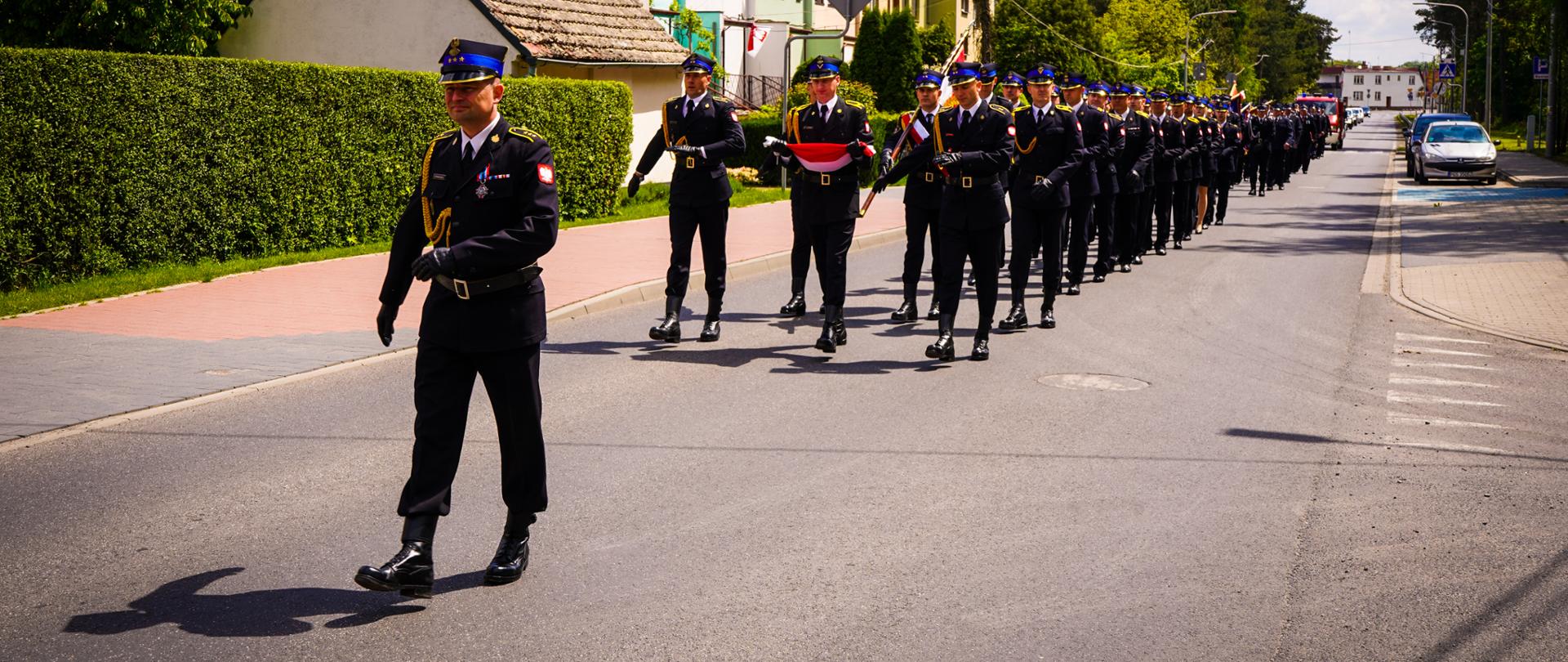 Strażacy idą w przemarszu podczas obchodów dnia strażaka.
