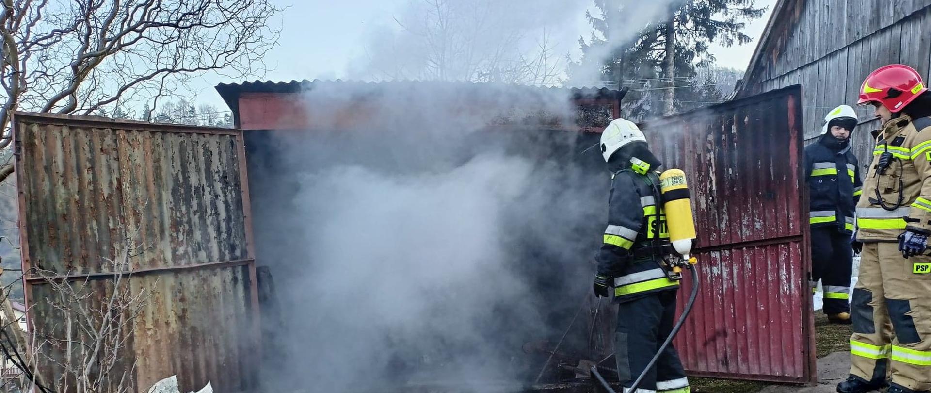 Strażacy gaszą pożar garażu. Z wnętrza wydobywa się dym.