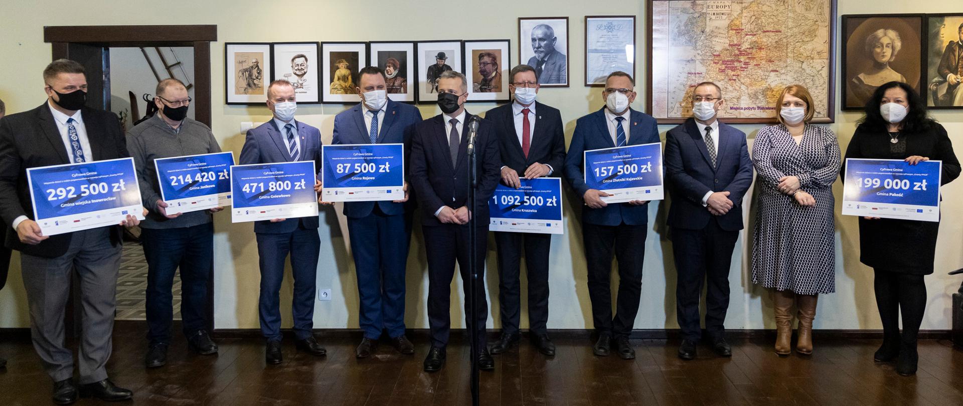 10 osób stojących na tle obrazów i portretów i trzymających vouchery