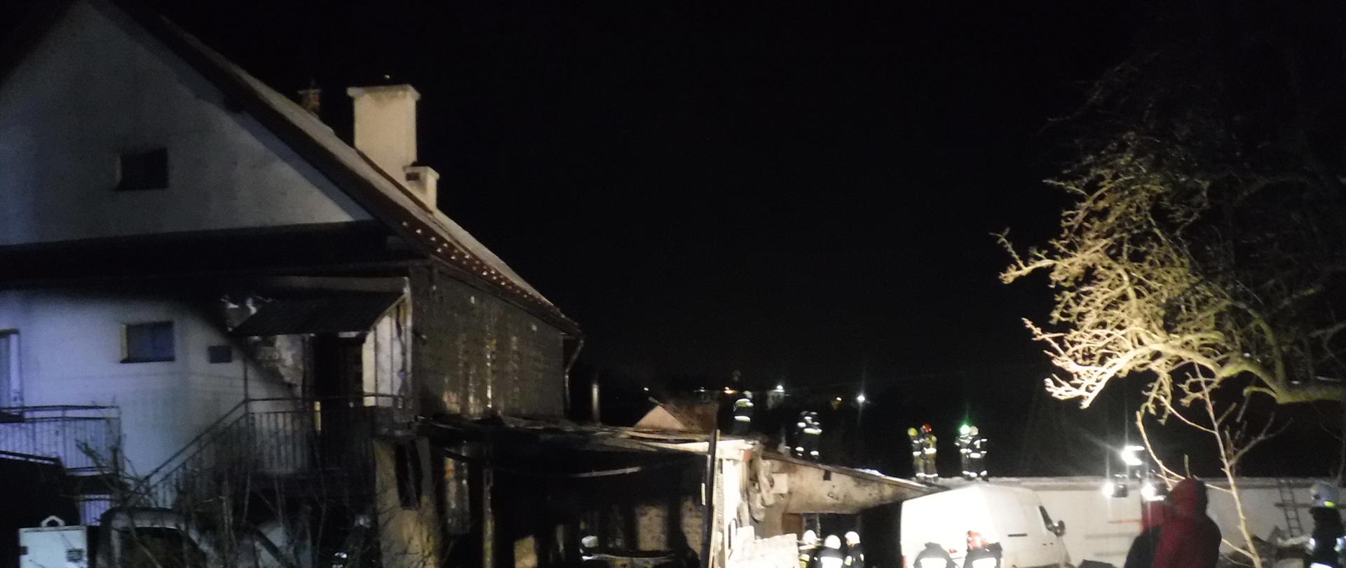 Murowany budynek jednorodzinny oraz przylegające bezpośrednio do niego budynki gospodarcze po ugaszeniu pożaru. Jest pora nocna. Miejsce zdarzenia jest oświetlone za pomocą najaśnić będących na wyposażeniu straży pożarnej przybyłej na miejsce zdarzenia. Przez teren prowadzonej akcji poprowadzone są linie wężowe, które służyły do podania środka gaśniczego na palące się obiekty. Strażacy znajdują się na dachu budynku gospodarczego oraz na terenie przed spalonymi obiektami , prowadząc prace rozbiórkowe. Ściana budynku mieszkalnego od strony przylegającego budynku gospodarczego jest silnie okopcona. Spaleniu uległa elewacja budynku mieszkalnego, sprzęt i wyposażenie budynku gospodarczego. W bliskiej odległości od budynku gospodarczego znajdują się dwa samochody dostawcze, które uległy częściowemu spaleniu. 