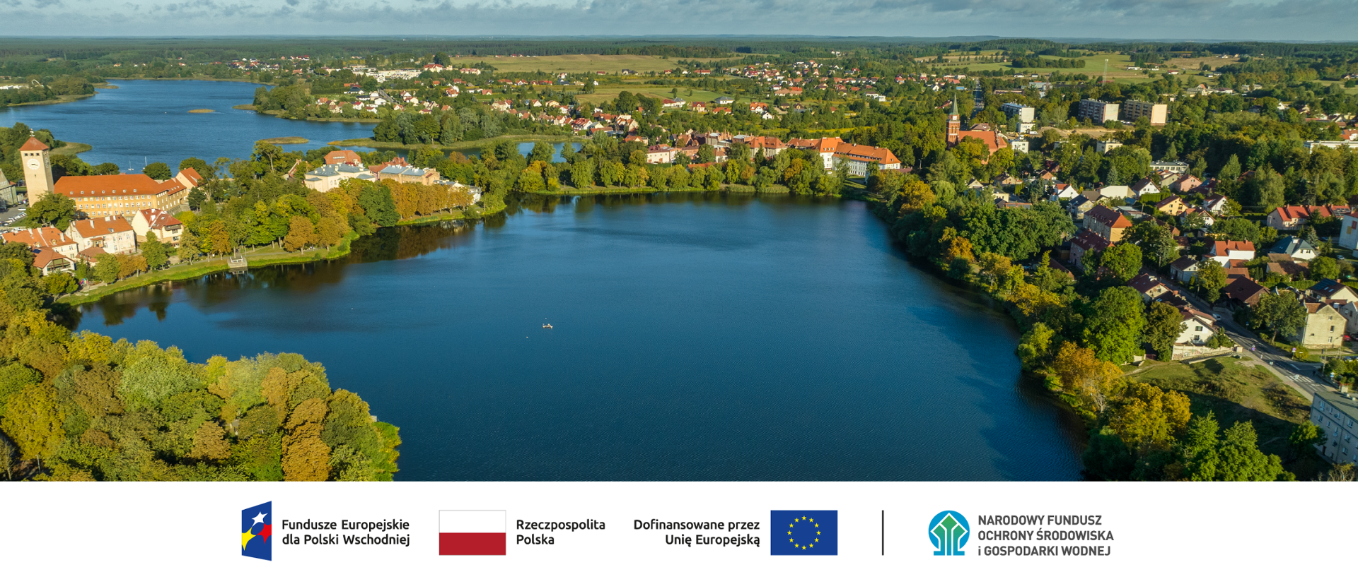 Zdjęcie krajobrazowe. Akwen wodny. Fot.: Urząd Gminy w Szczytnie. Ciąg znaków, logotypy od lewej: FEdPW flaga Rzeczypospolita Polska, flaga UE Dofinansowane przez UE, NFOŚiGW.
