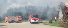 Widoczne pojazdy gaśnicze, strażacy i zadymiony budynek inwentarski