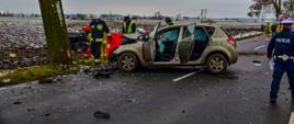 Rozbite dwa samochody osobowe. Kia Ceed stojąca w poprzek drogi, mercedes w polu wokół którego strażacy udzielają pomocy poszkodowanym.