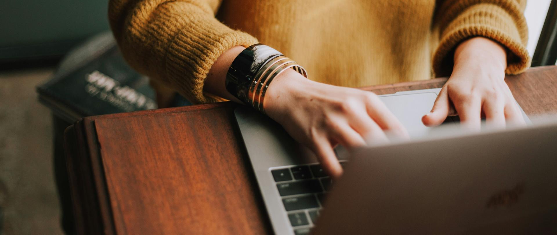 Laptop leżący na biurku, dłonie kobiety położone na laptopie