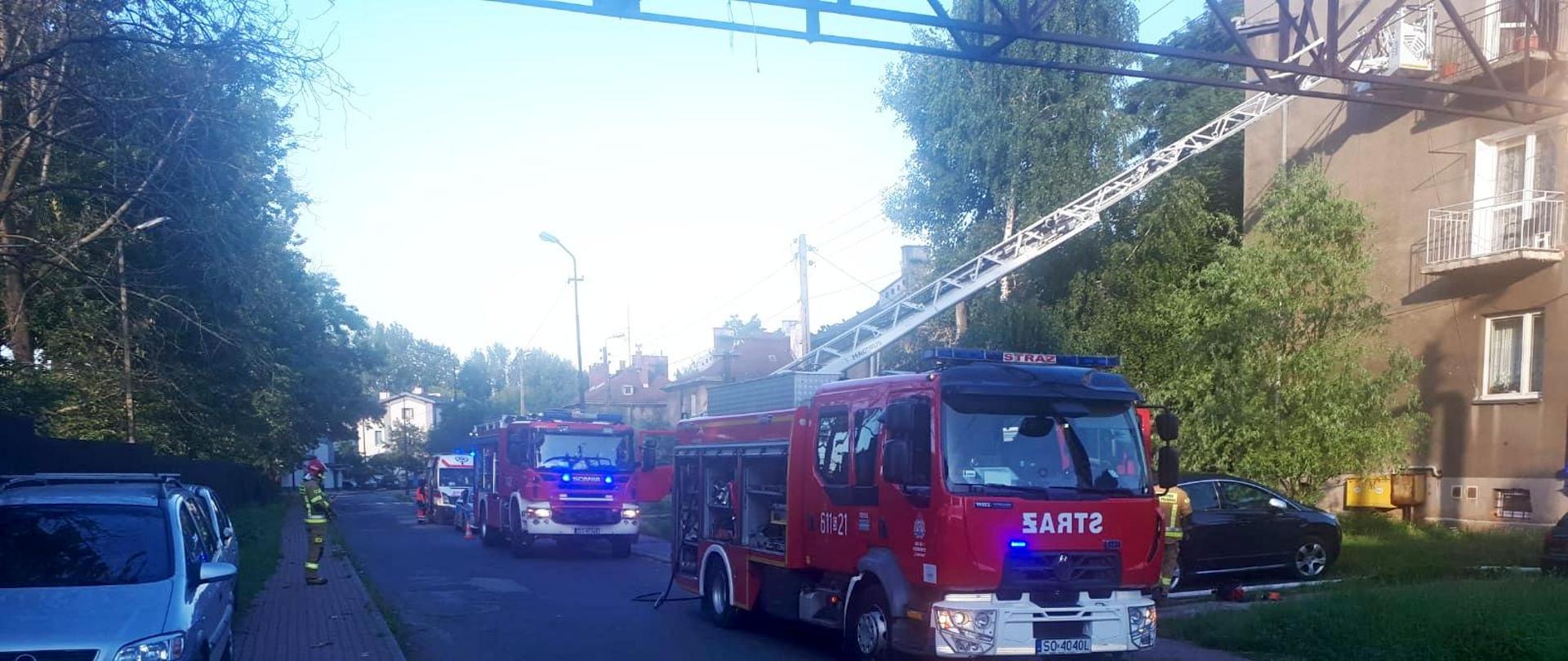 Zdjęcie przedstawia pojazdy pożarnicze ustawione na ulicy przy domu wielorodzinnym podczas akcji ratowniczo - gaśniczej 