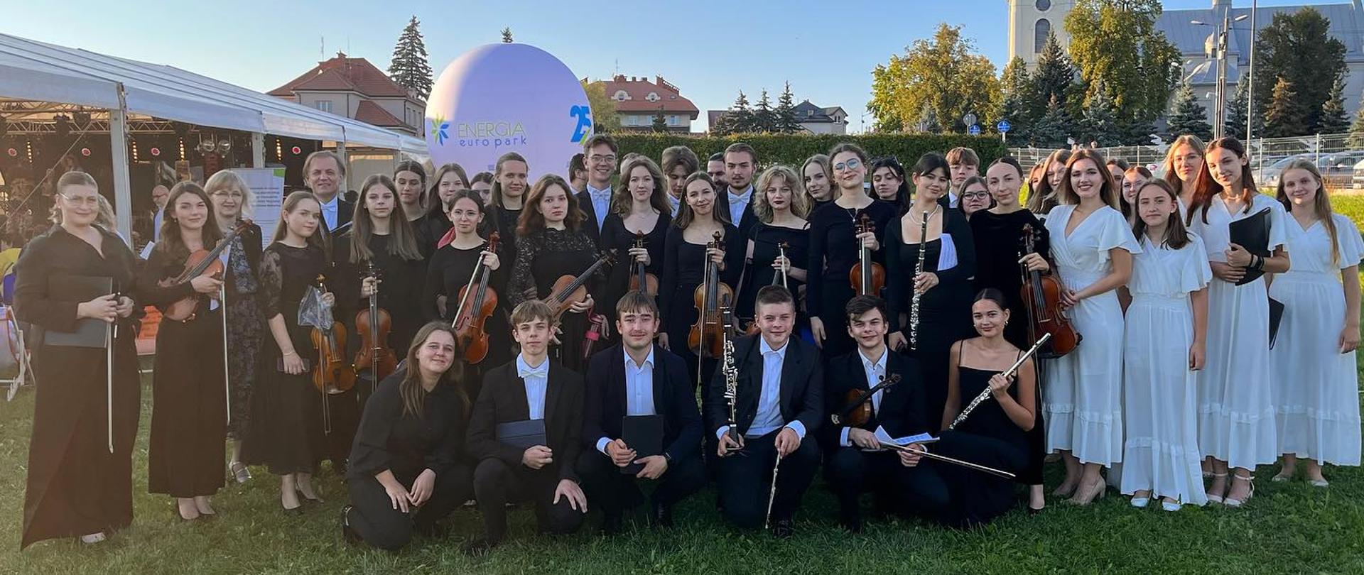 orkiestra symfoniczna PSM Mielec II stopnia oraz chór projektowy na tle mieleckiej starówki i bazyliki mniejszej pod wezwaniem św. Mateusza w Mielcu podczas koncertu na bulwarach