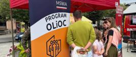 Podlascy strażacy #PSP i #OSP czynnie włączyli się w trening, przekazując informacje dotyczące bezpieczeństwa. Na zdjęciu strażacy przekazują treści dotyczące bezpieczeństwa, w tle namioty pod którymi leżą elementy wyposażenia plecaka ewakuacyjnego. Wszystkiemu przygląda się ludność cywilna. Całość odbywa się na podwórku. 