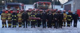 Strażacy JRG Miechów oraz Komendy Powiatowej PSP w Miechowie na tle samochodów ratowniczo - gaśniczych w umundurowaniach służbowych.