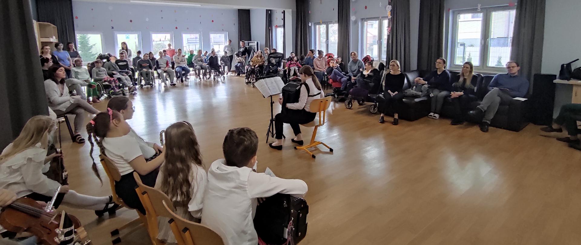 Zdjęcie przedstawia koncert w sali. Na srodku dziecko gra na akordeonie.Wokoło solisty siedzą słuchacze w tym podopieczni Centrum Edukaji i Terapii w Piszu.
