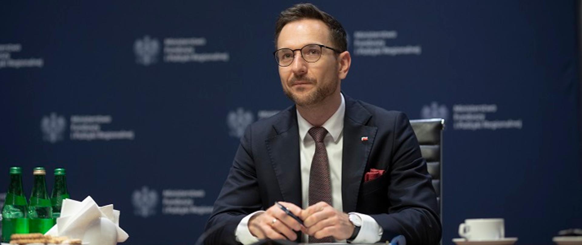 Wiceminister Waldemar Buda siedzi za stołem konferencyjnym, w tle ścianka z logo MFiPR