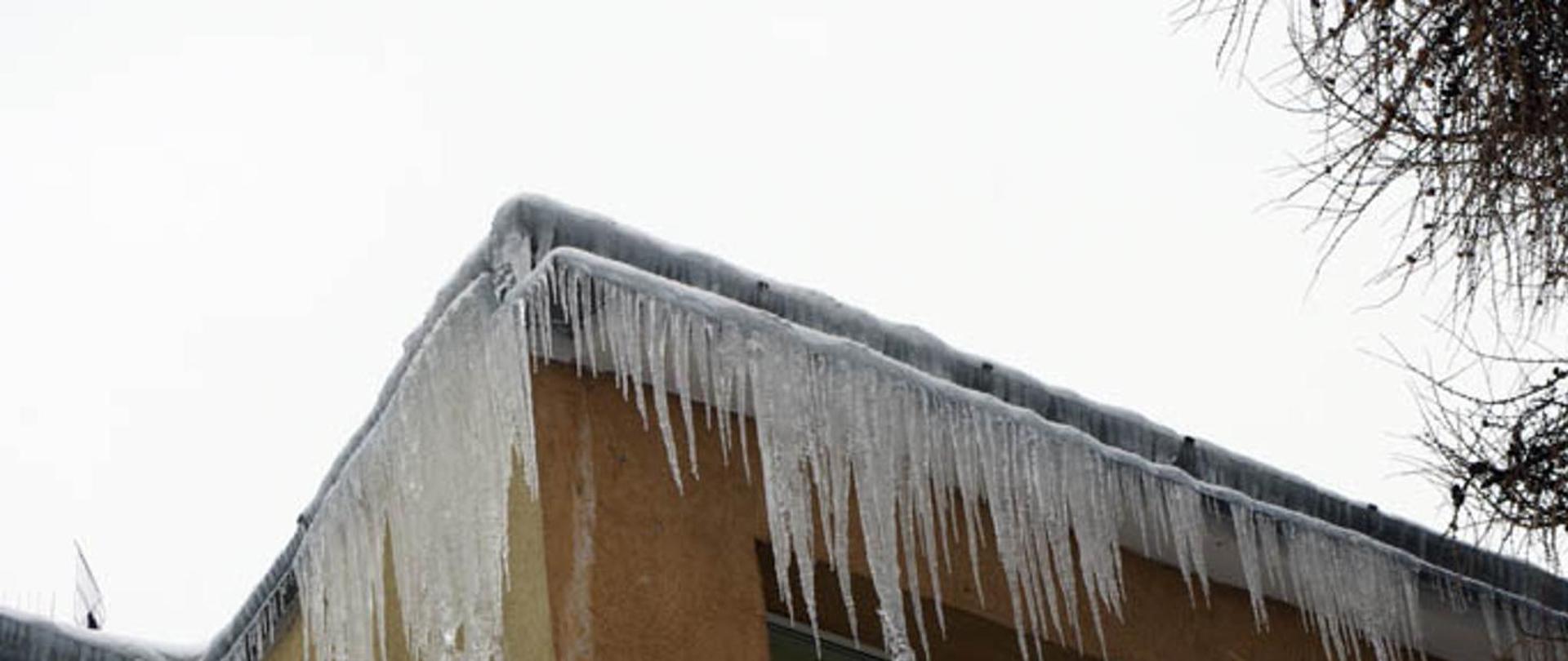 Zdjęcie przedstawia sople lodu zwisające z dachu budynku