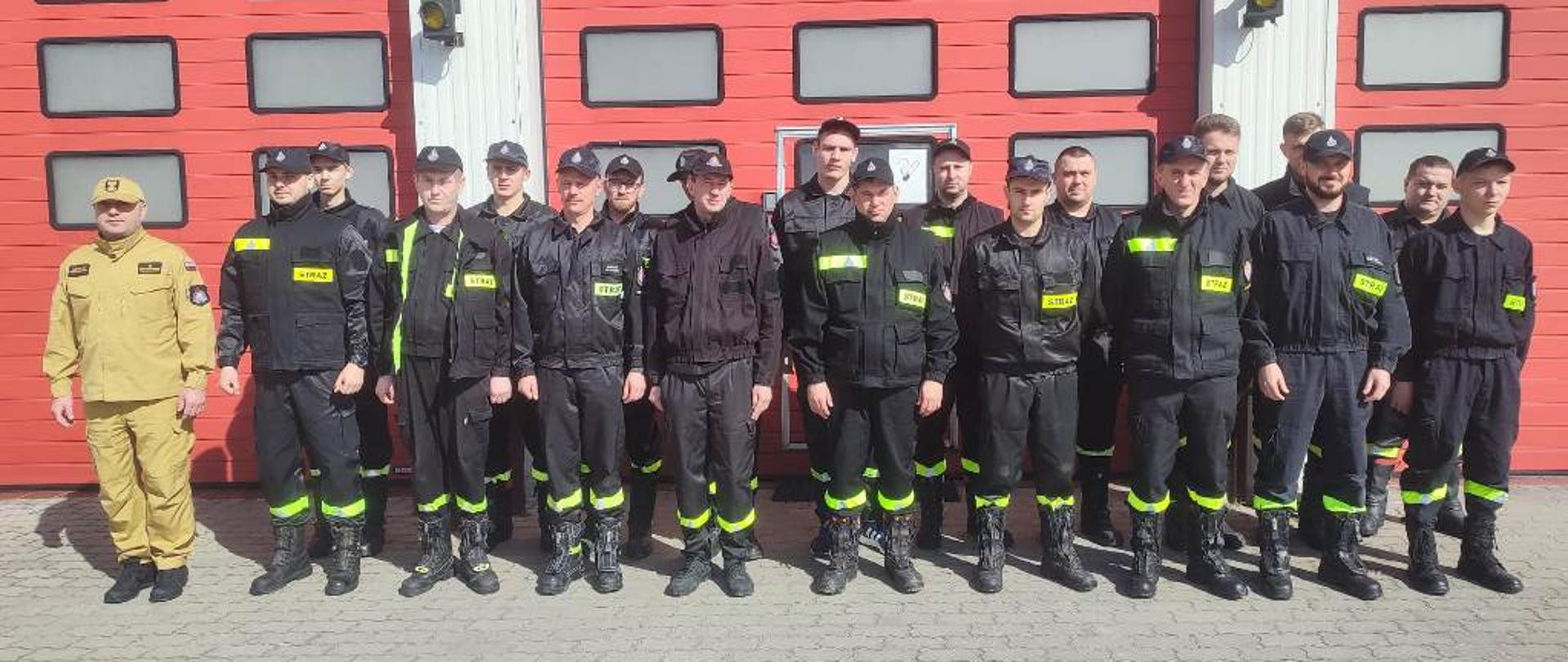 Plac wewnętrzny KP PSP, grupowe zdjęcie uczestników kursu na tle garaży komendy