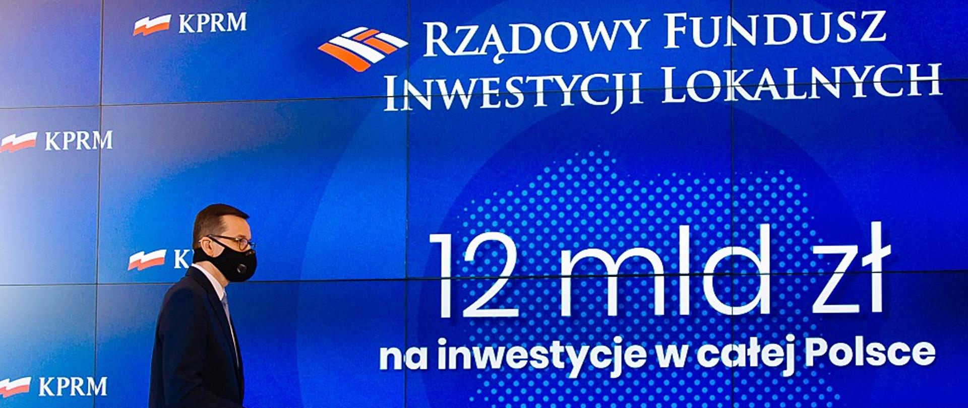Premier Mateusz Morawiecki na tle ścianki wizyjnej.
