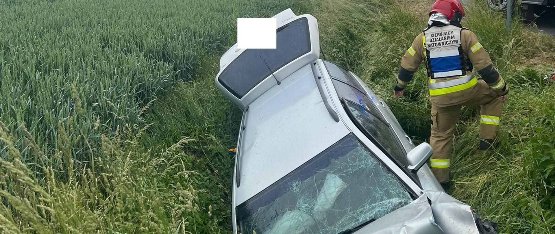 Samochód osobowy rozbity leży w rowie, z rowu wychodzi strażak