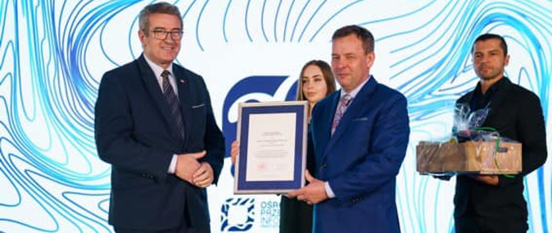 Jubileusz Ośrodka Przetwarzania Informacji – Państwowego Instytutu Badawczego z udziałem wiceministra Wojciecha Murdzka, wiceminister Wojciech Murdzek wraz z uczestnikami uroczystości na scenie.