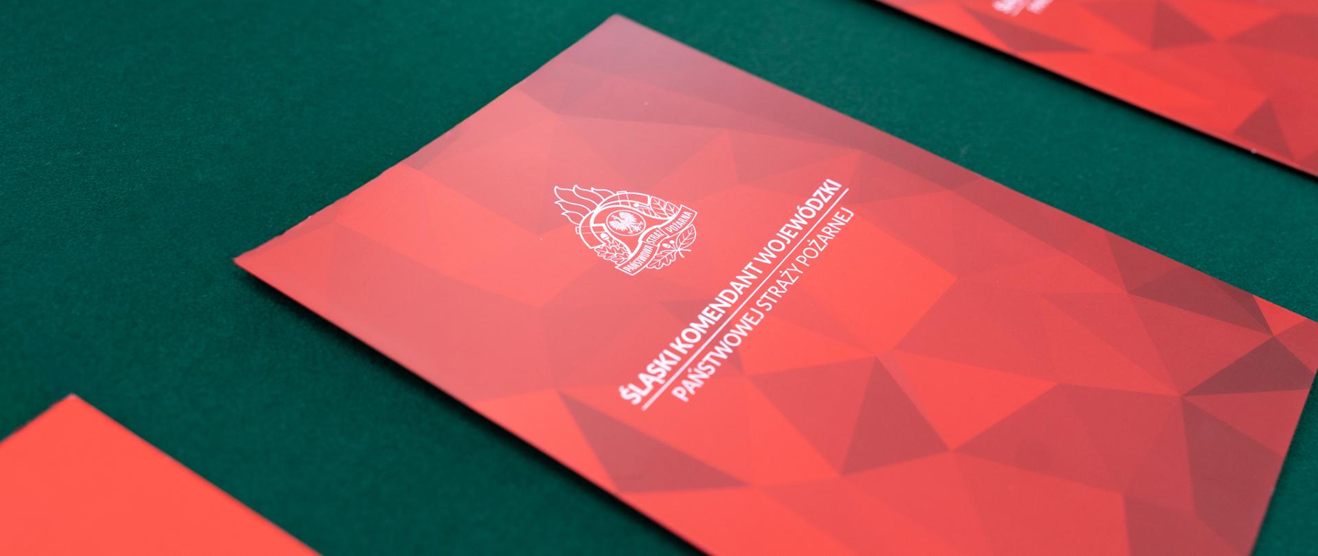 Na zdjęciu widać teczki w kolorze czerwonym leżące na zielonym tle.