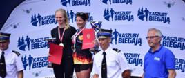 Na podium stoją zwyciężczynie biegu w obecności komendanta powiatowego PSP w Pucku, organizatora biegu PSP i OSP z ramienia Komendy Wojewódzkiej PSP oraz organizatora cyklu biegów "Kaszuby Biegają".