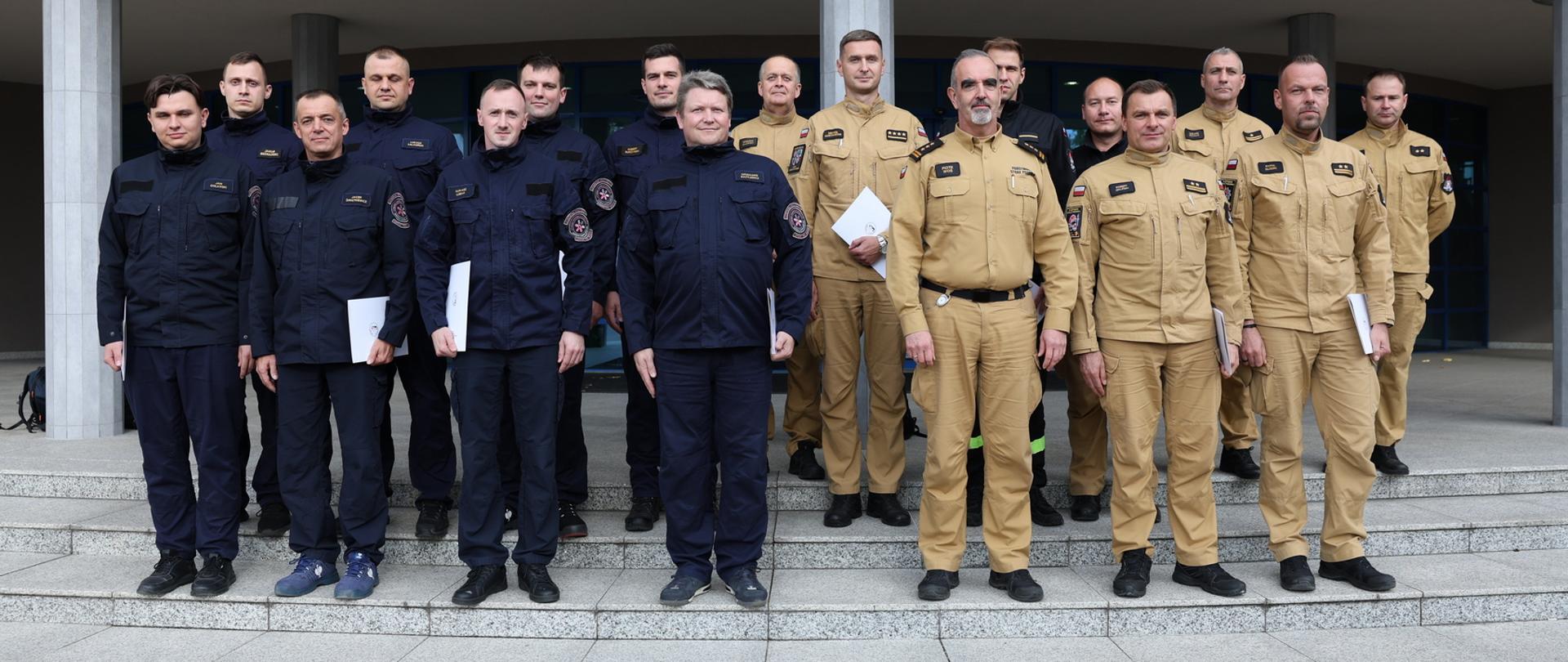 Pamiątkowe zdjęcie grupowe funkcjonariuszy PSP oraz Lotniskowej Straży Pożarnej (15 osób) z okazji ukończenia szkolenia w towarzystwie Zastępcy Komendanta Centralnej Szkoły PSP oraz funkcjonariusza CS PSP