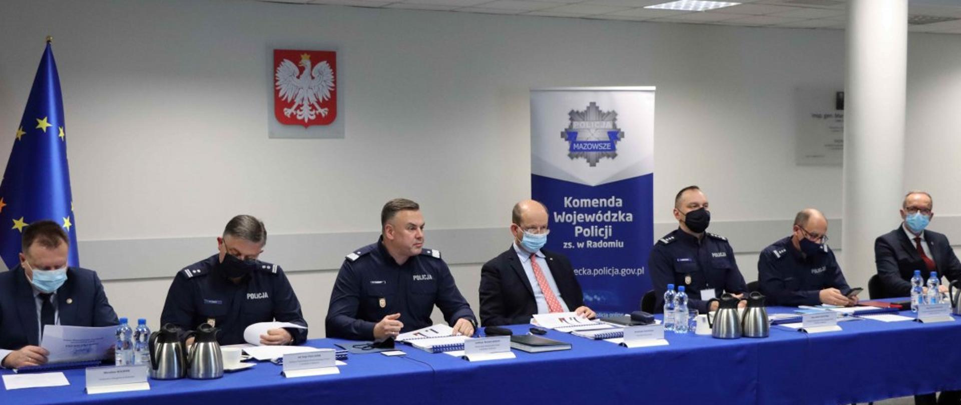 Grupa policjantów i urzędników siedzących przy stole. 