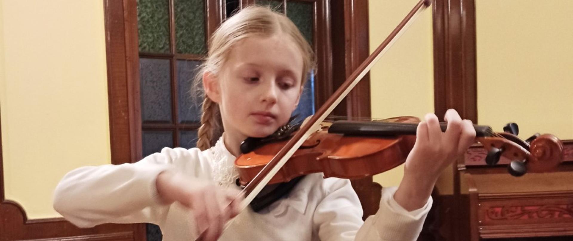 Zdjęcie kolorowe. Dziewczynka w białej bluzce gra na skrzypcach.