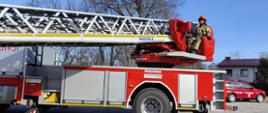 Samochód pożarniczy z drabiną mechaniczną wraz z operatorem drabiny ubranym w ubranie typu NOMEX oraz czerwony hełm