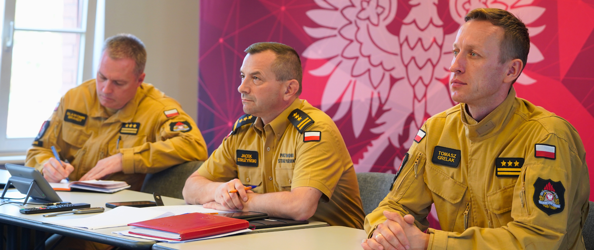Strażacy zajmują miejsca za stołem w sali prezydialnej komendy, biorąc udział w wideokonferencji z Komendą Główną PSP.