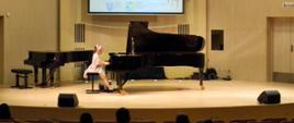 Galeria 7 zdjęć z I Ogólnopolskiego Konkursu Pianistycznego "Fortepian Żywcem brzmiący", który odbył się w dniach 20-21.03.2025. Młoda uczennica gra na fortepianie na scenie sali koncertowej.