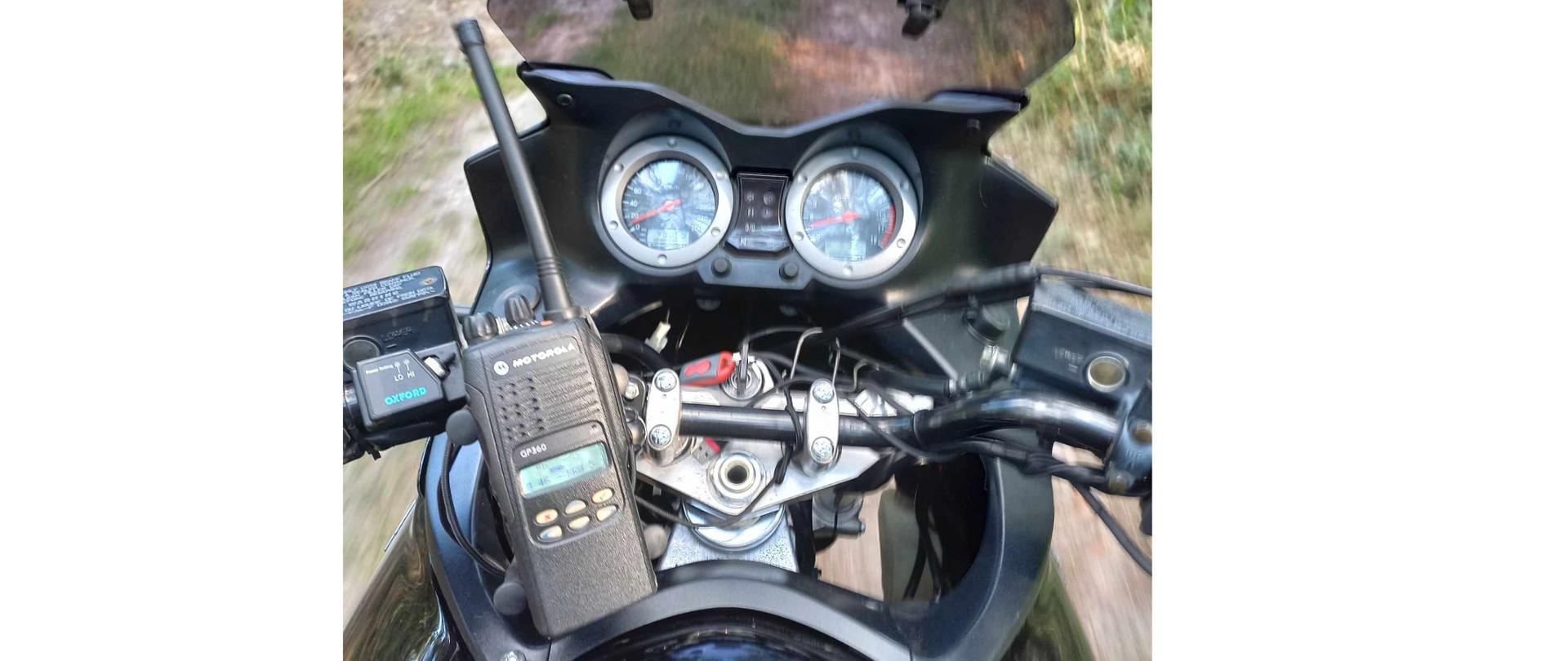 Widok zegarów motocykla na których leży radiostacja nasobna