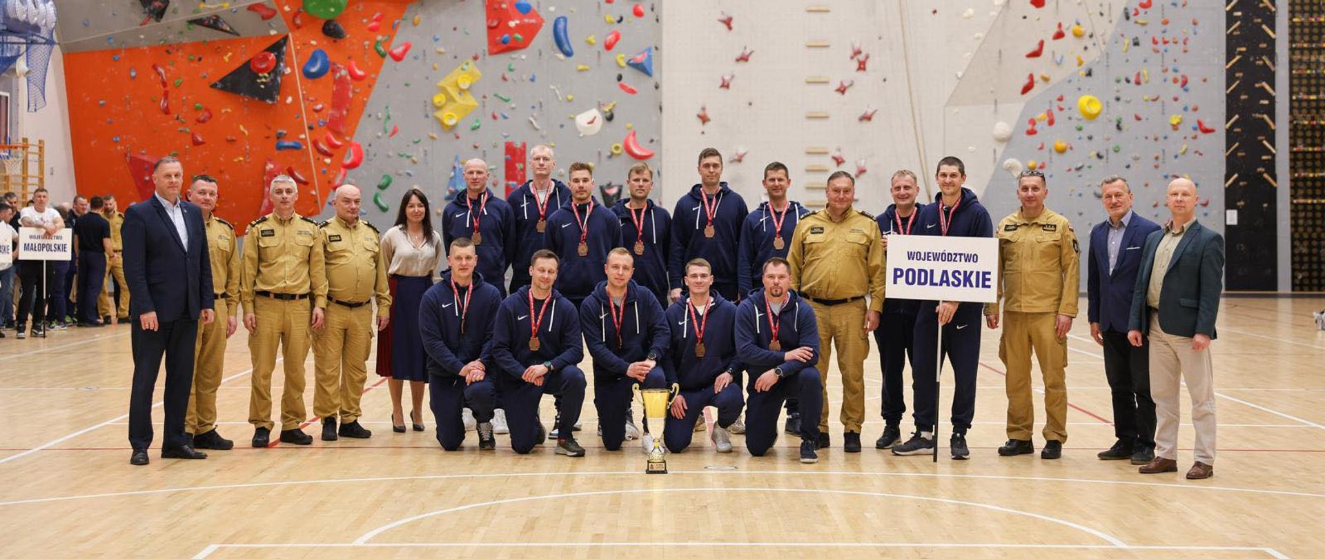 Zakończenie 41. Mistrzostw Polski Strażaków w Piłce Siatkowej - drużyna podlaskich siatkarzy, w tle hala sportowa i ścianka wspinaczkowa