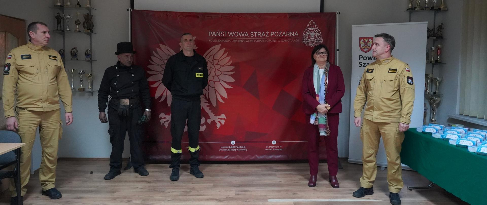 Starosta powiatu szamotulskiego, komendant powiatowy, funkcjonariusz straży i kominiarz na świetlicy, za nimi czerwony baner PSP