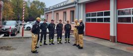 Strażacy przed budynkiem strażnicy KP PSP w Kościanie. Strażacy stoją w półkolu i rozmawiają.