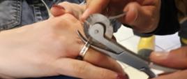 Strażak ręczną piłą przecina obrączkę na palcu serdecznym pacjentki. Ręka leży na kolanie.