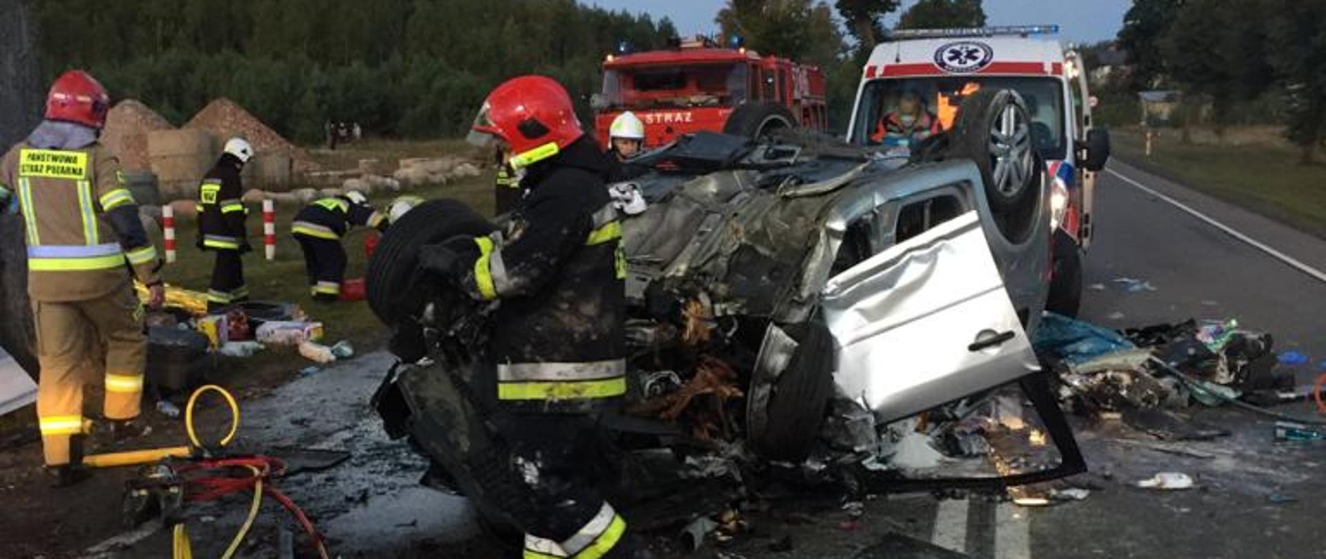 Zdjęcie przedstawia zniszczony samochód po wypadku, służby ratownicze podczas prowadzonych zajęć