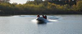 Akwen, na nim - na pontonie trzech strażaków. Ponton płynie w kierunku brzegu. W tle trzciny, zarośla i las.
