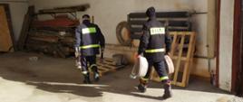 Widoczni strażacy w garażu komendy noszący i układający sprzęt pożarniczy oddany przez ochotnicze straże pożarne