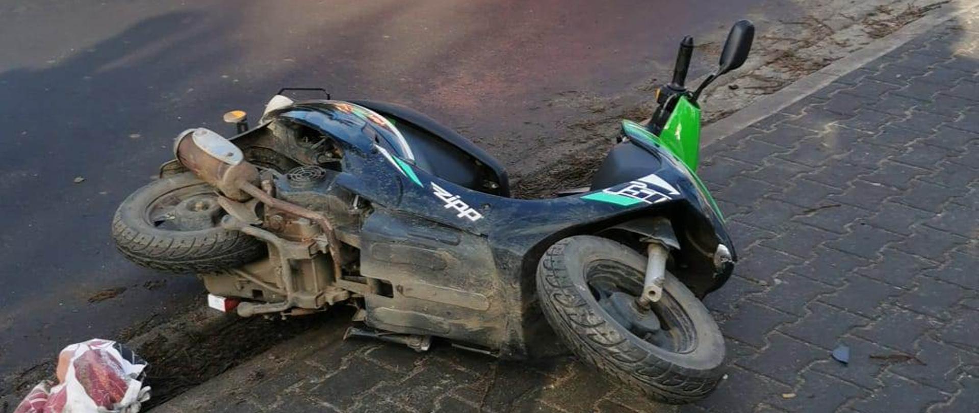 Widać leżący skuter na chodniku, za nim samochód strażacki