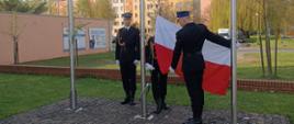 Zdjęcie przedstawia mocowanie i wciągnięcie na masz flagi państwowej przez poczet flagowy przed Komendą Powiatową PSP w Wałczu 