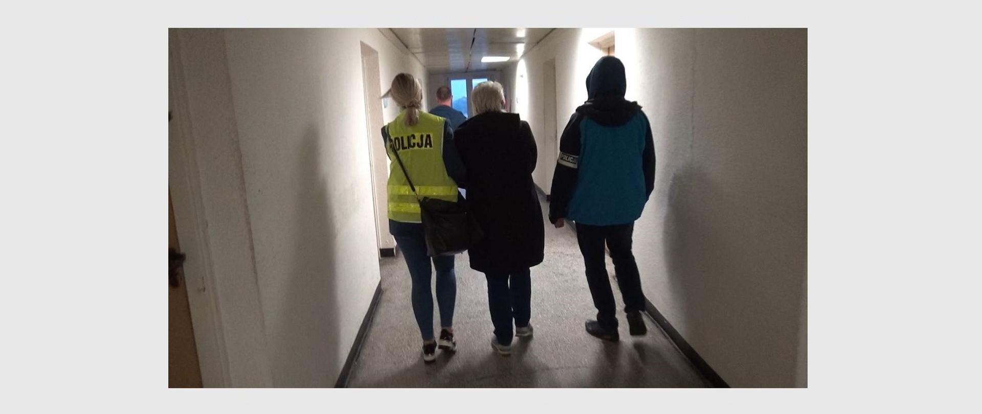 zdjęcie przedstawiające zatrzymaną kobietę oraz funkcjonariuszy policji w korytarzu budynku