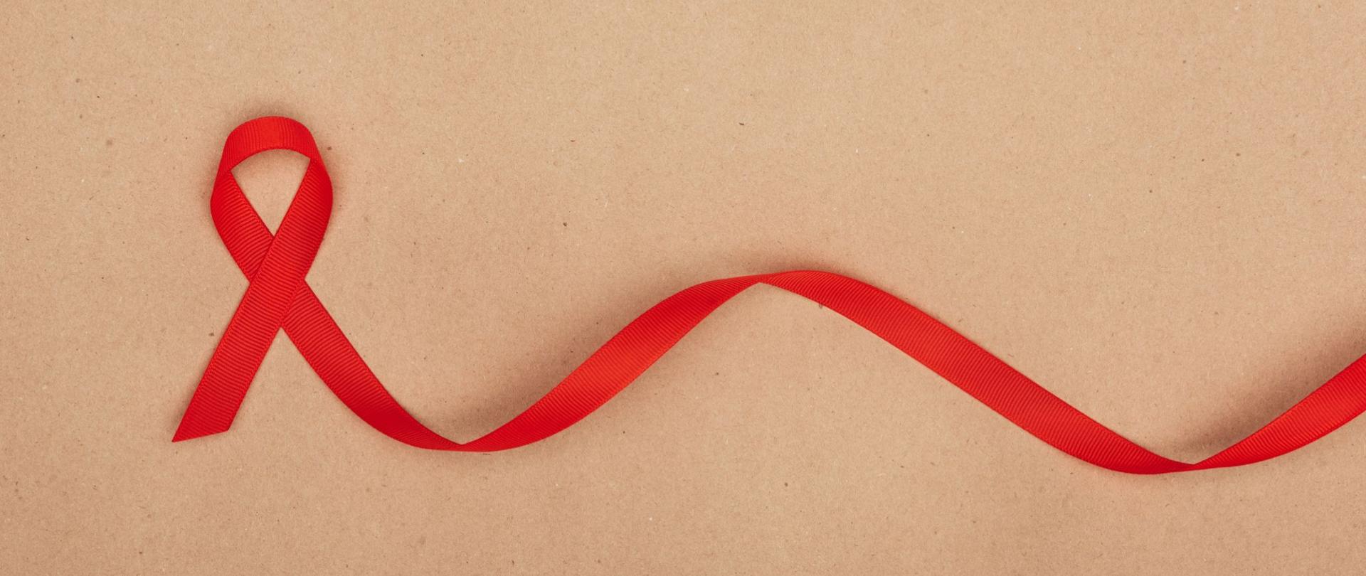 Na zdjęciu jest czerwona wstążka. Tło jest beżowe.
