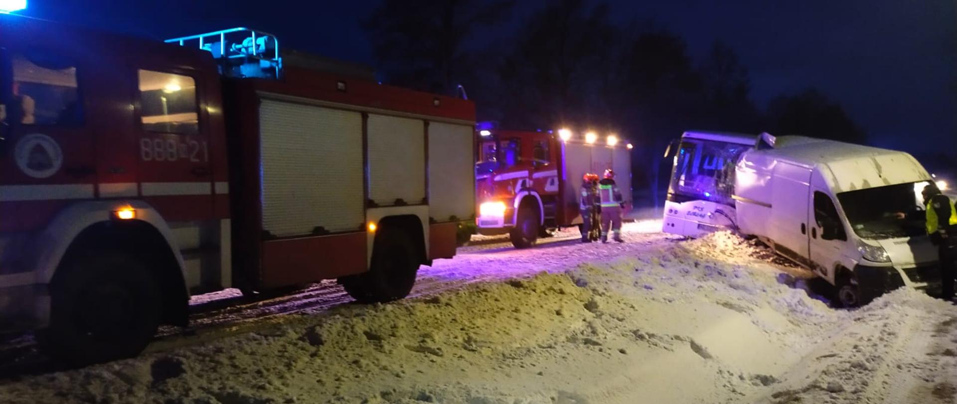 Zima, białe zaśnieżone drogi i pobocza. Z prawej strony biały bus na poboczu w który uderzył autobus, oba poza drogą. Z lewej strony zdjęcia na drodze ustawione samochody strażackie