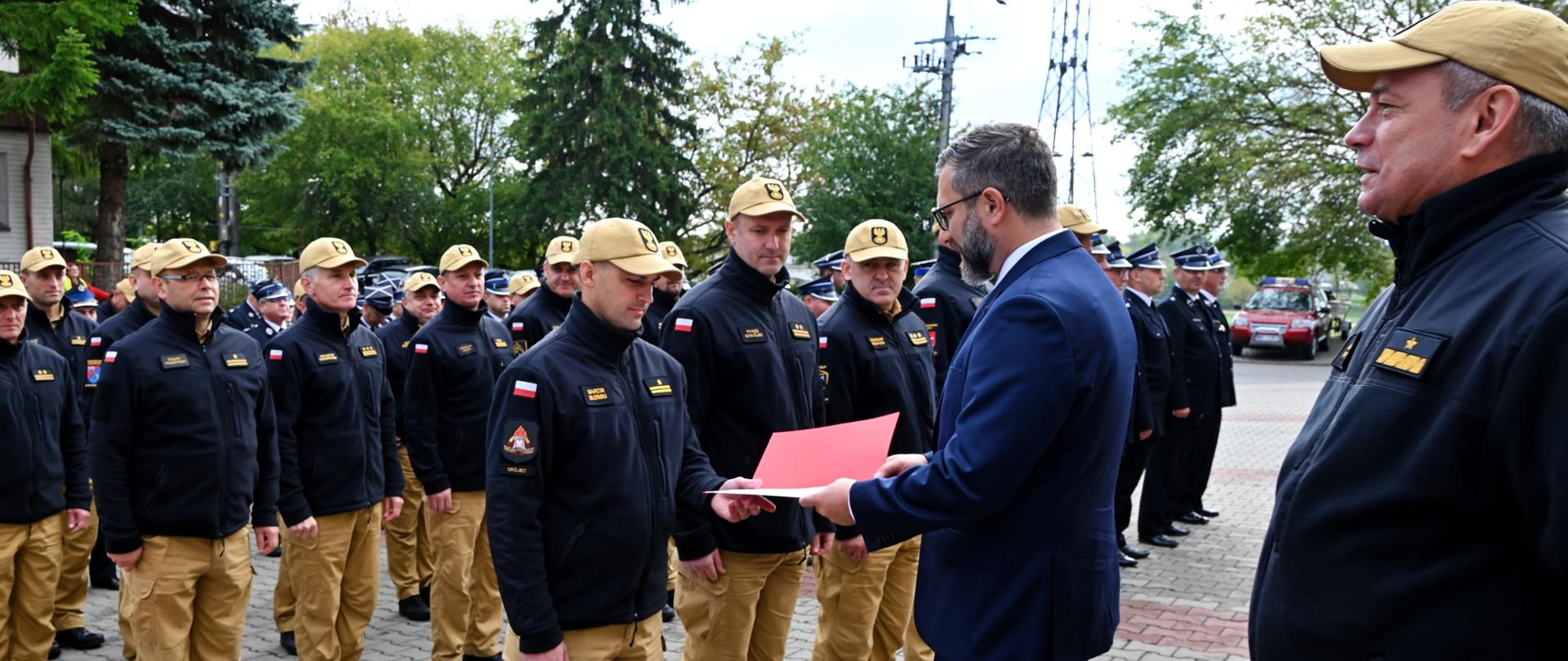 strażacy stoją na placu podczas Przekazania agregatów prądotwórczych dla jednostek PSP i OSP z terenu województwa mazowieckiego