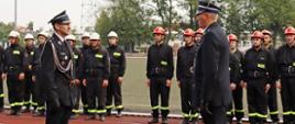 dowódca uroczystości składa meldunek prezesowi związku ochotniczych straży pożarnych ubrani są w galowe strażackie stroje w tle znajdują się ustawione w dwuszeregach drużyny męskie