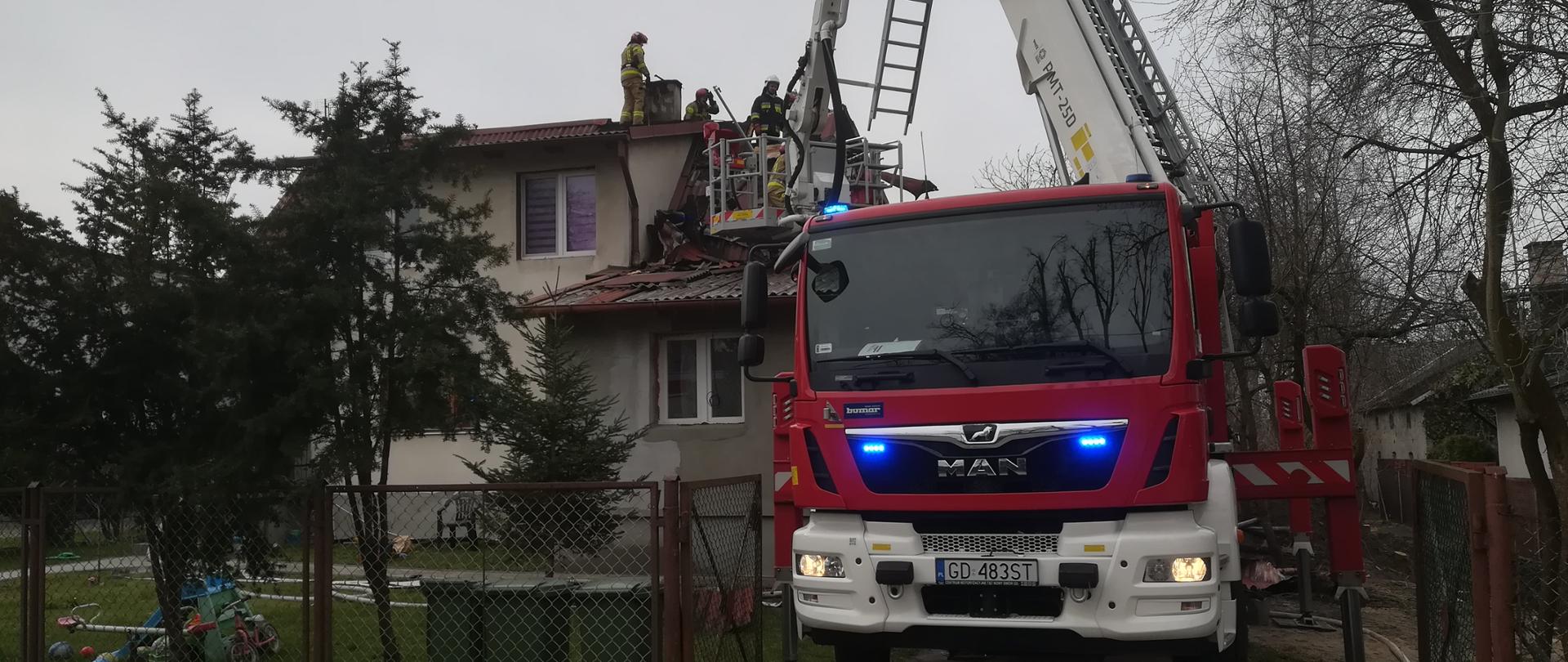Na zdjęciu podnośnik SHD21 przy budynku, strażacy pracujący na dachu budynku mieszkalnego.