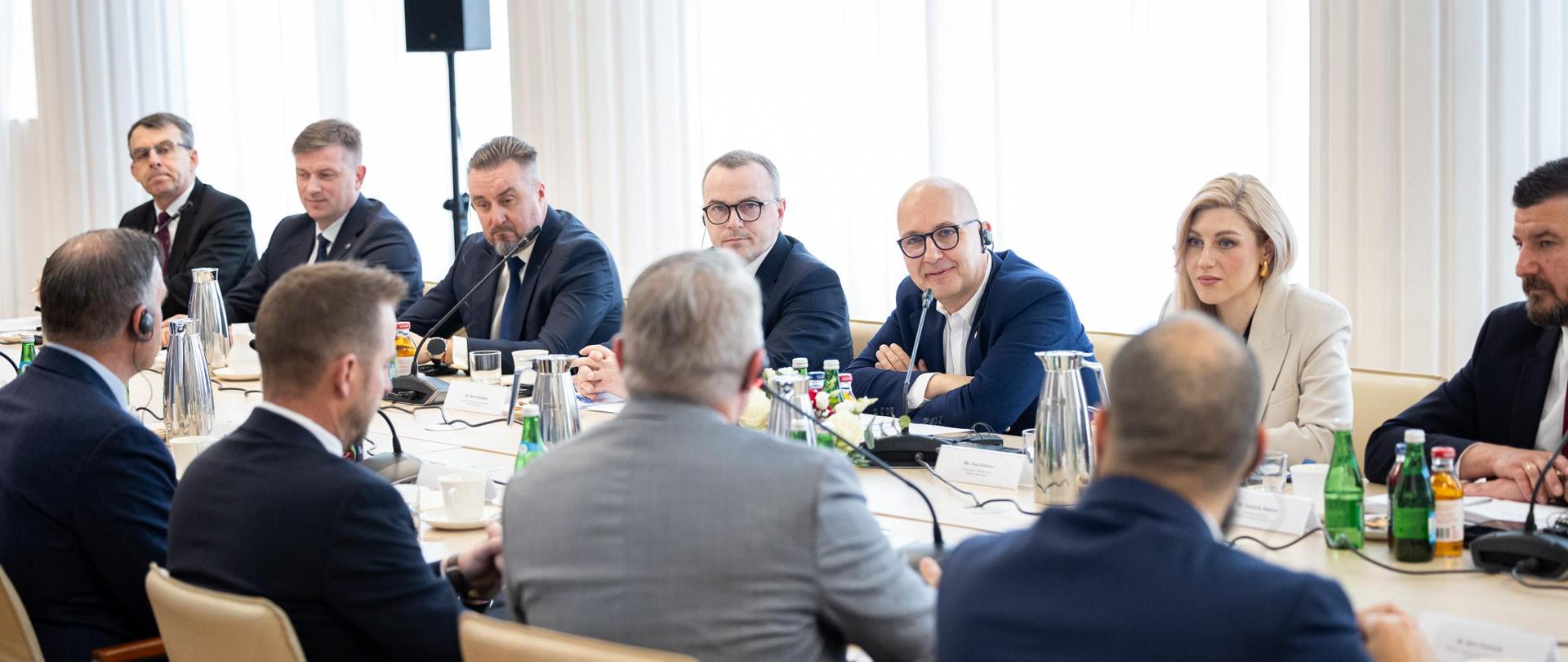 Wiceminister Robert Kropiwnicki wraz z przedstawicielami MAP, siedzą przy stole podczas spotkania z przedstawicielami amerykańskiego przemysłu obronnego. Na stole dzbanki, butelki z wodą, słuchawki, mikrofony oraz kwiaty. Na pierwszym planie przedstawiciele amerykańskiego przemysłu obronnego siedzący tyłem.